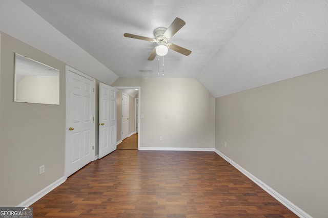 additional living space with dark wood-style floors, vaulted ceiling, a textured ceiling, and baseboards