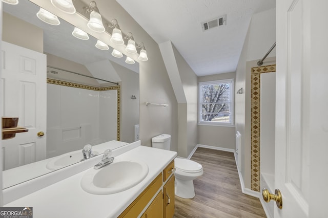 bathroom featuring toilet, wood finished floors, vanity, visible vents, and a shower