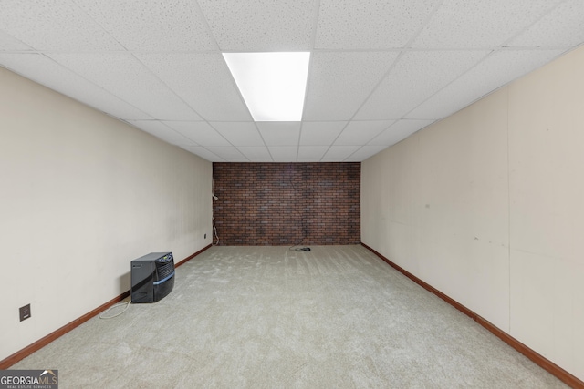 finished below grade area with baseboards, a drop ceiling, light carpet, and brick wall