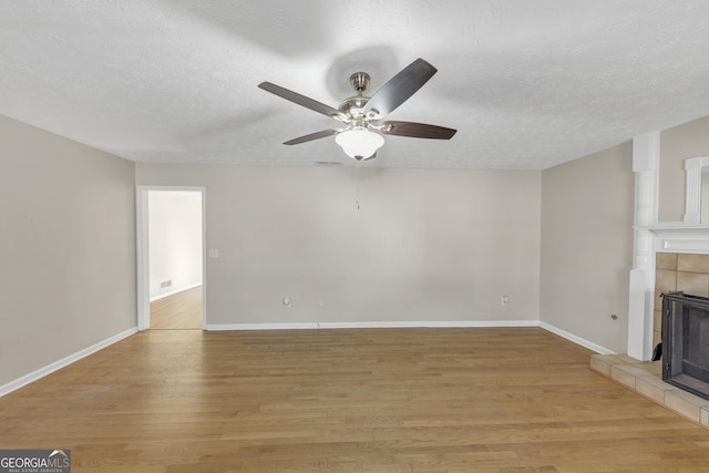 unfurnished living room with baseboards, a fireplace, light wood-style flooring, and a textured ceiling