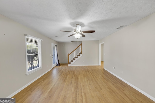 unfurnished living room featuring baseboards, visible vents, a ceiling fan, stairs, and light wood-style floors