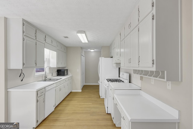 kitchen featuring light wood finished floors, light countertops, white cabinets, a sink, and white appliances