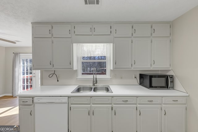 kitchen featuring light countertops, white cabinetry, white dishwasher, a sink, and black microwave