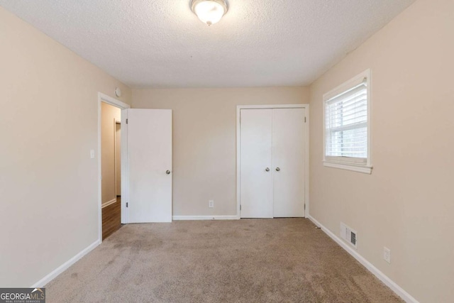 unfurnished bedroom featuring light carpet, a closet, a textured ceiling, and visible vents