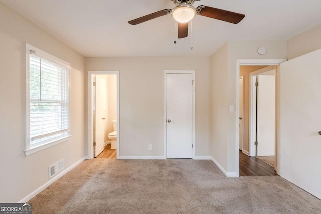 unfurnished bedroom featuring visible vents, baseboards, a ceiling fan, light colored carpet, and ensuite bath