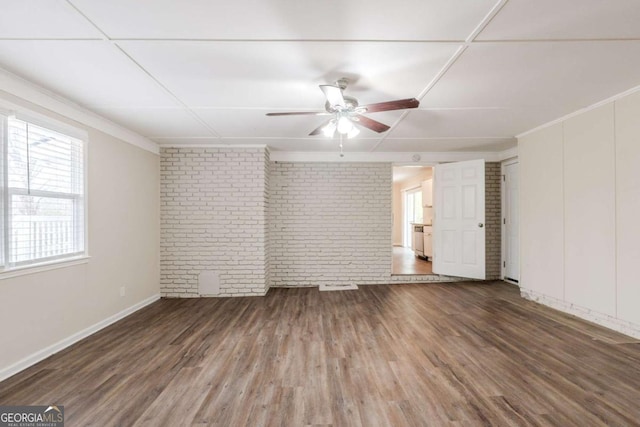 unfurnished room with baseboards, brick wall, ceiling fan, ornamental molding, and dark wood-style flooring