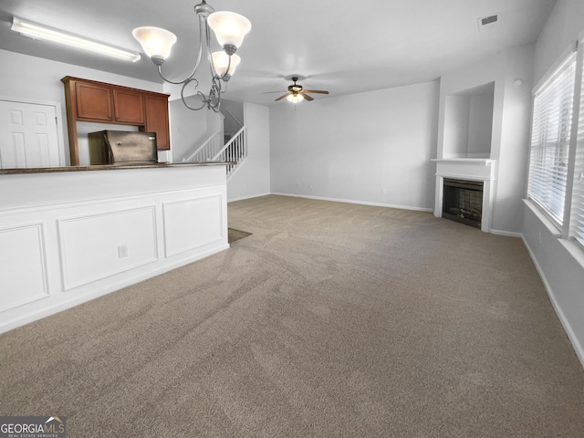 unfurnished living room featuring light carpet, visible vents, baseboards, stairway, and a fireplace