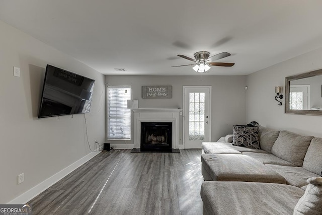 unfurnished living room with a fireplace, wood finished floors, a ceiling fan, visible vents, and baseboards