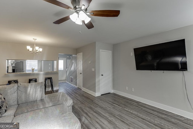 living room featuring ceiling fan with notable chandelier, visible vents, baseboards, and wood finished floors