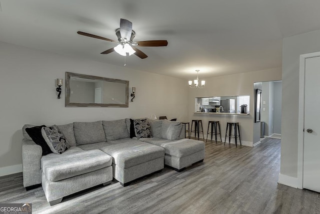 living area featuring ceiling fan with notable chandelier, baseboards, and wood finished floors