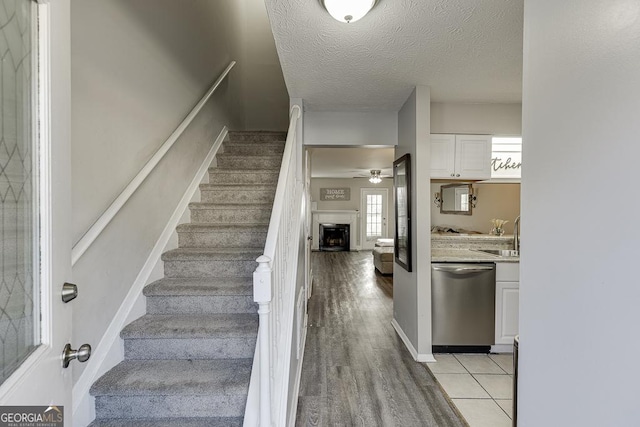 staircase with a fireplace, a ceiling fan, a textured ceiling, tile patterned flooring, and baseboards