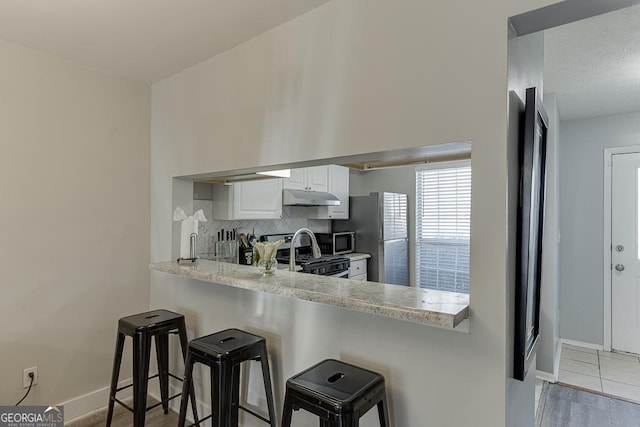 kitchen featuring a breakfast bar area, decorative backsplash, appliances with stainless steel finishes, white cabinets, and under cabinet range hood