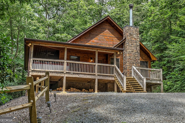 rustic home featuring ceiling fan, a chimney, a wooden deck, and stairs