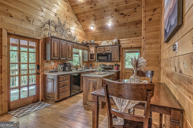 kitchen with black appliances, light wood-style flooring, a kitchen island, and wooden walls