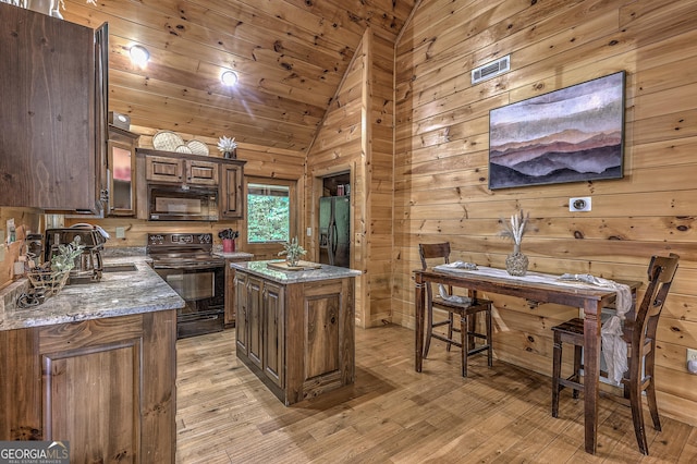 kitchen with light wood-style flooring, a center island, vaulted ceiling, light stone countertops, and black appliances