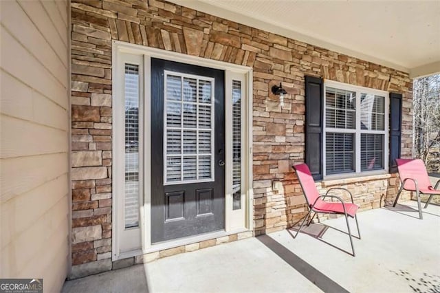 doorway to property with a porch, stone siding, and brick siding