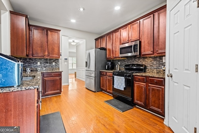 kitchen with light wood finished floors, appliances with stainless steel finishes, dark stone counters, and decorative backsplash