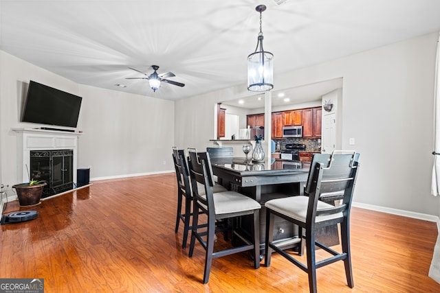 dining area featuring light wood finished floors, a fireplace, baseboards, and a ceiling fan