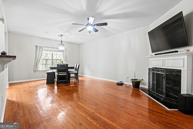 dining room featuring a fireplace, wood finished floors, a ceiling fan, and baseboards