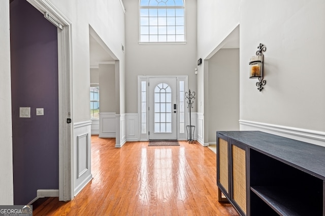 entryway with wainscoting, light wood-style flooring, and a high ceiling