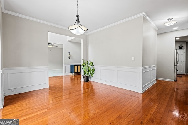 unfurnished dining area with a ceiling fan, a wainscoted wall, ornamental molding, and wood finished floors