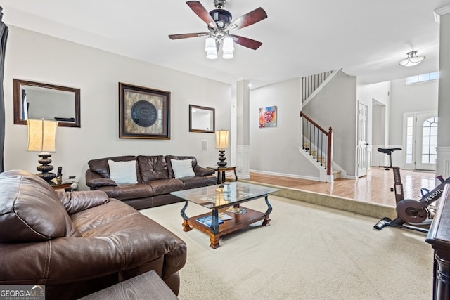 living area featuring a ceiling fan, baseboards, and stairs