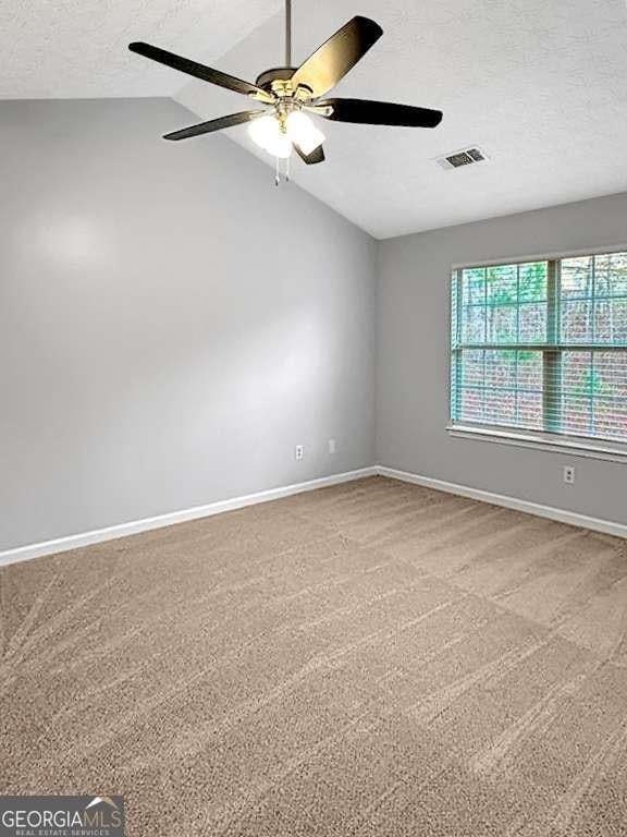 carpeted empty room with lofted ceiling, a textured ceiling, a ceiling fan, visible vents, and baseboards