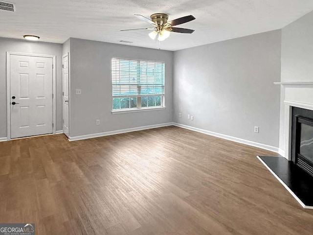 unfurnished living room with wood finished floors, a glass covered fireplace, visible vents, and baseboards