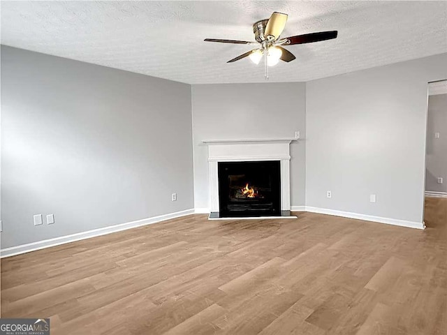 unfurnished living room featuring light wood finished floors, a warm lit fireplace, baseboards, and a textured ceiling