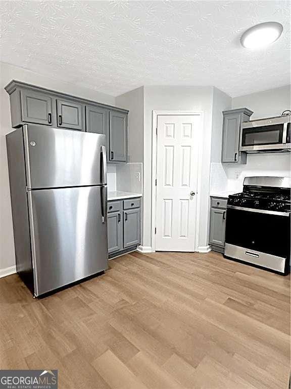 kitchen with a textured ceiling, light wood-style flooring, stainless steel appliances, light countertops, and gray cabinets