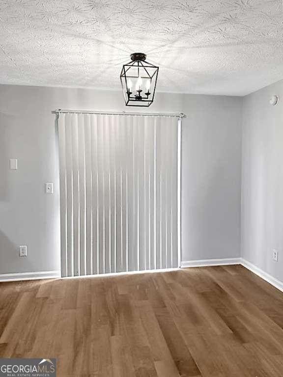 unfurnished dining area with a notable chandelier, a textured ceiling, baseboards, and wood finished floors