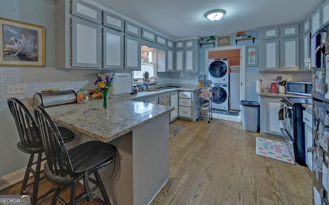 kitchen featuring stacked washer and clothes dryer, stainless steel microwave, a peninsula, and a kitchen bar