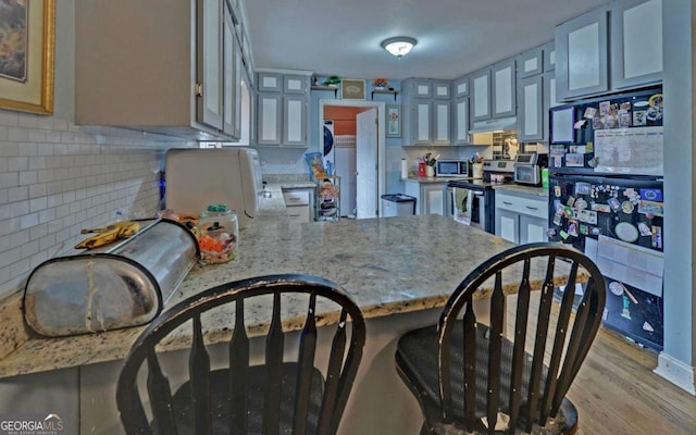 kitchen featuring stainless steel appliances, gray cabinetry, a peninsula, and decorative backsplash