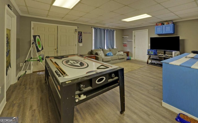 rec room with ornamental molding, a drop ceiling, light wood-style flooring, and baseboards