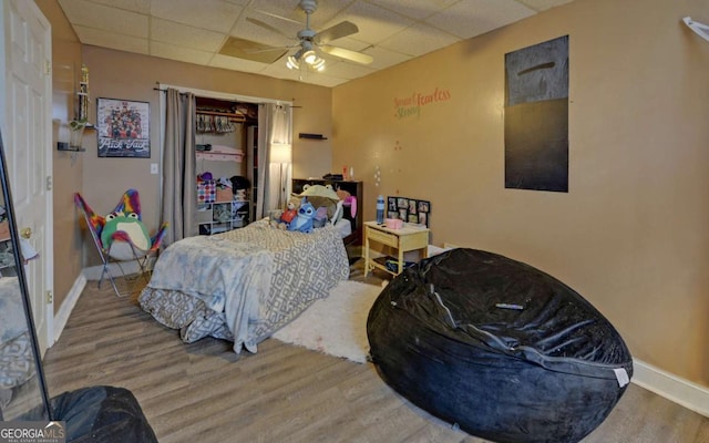 bedroom with a paneled ceiling, ceiling fan, baseboards, and wood finished floors