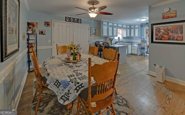 dining room with light wood finished floors, a ceiling fan, baseboards, and crown molding