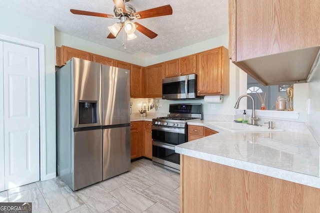 kitchen with brown cabinetry, stainless steel appliances, a textured ceiling, light countertops, and a sink