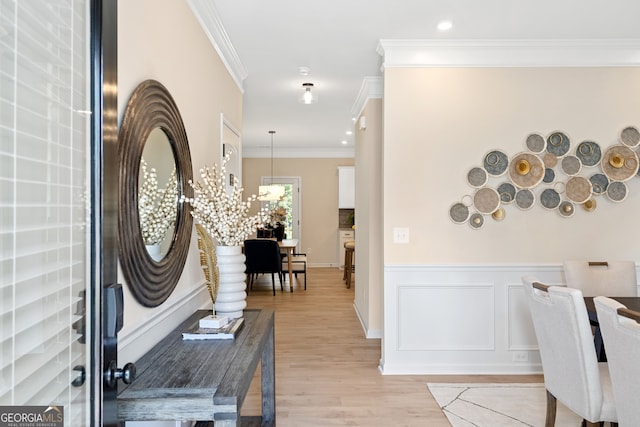 foyer entrance with ornamental molding, a wainscoted wall, light wood-style floors, and a decorative wall