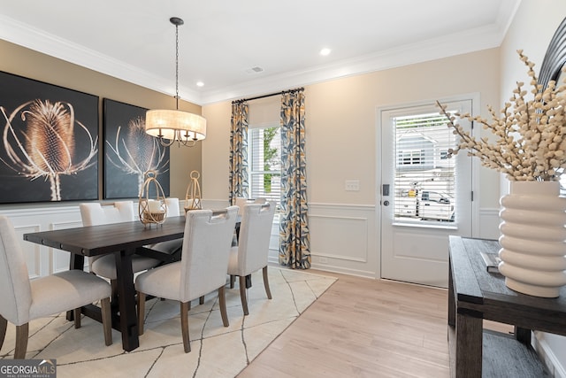 dining area featuring a wainscoted wall, crown molding, a decorative wall, light wood-style flooring, and an inviting chandelier