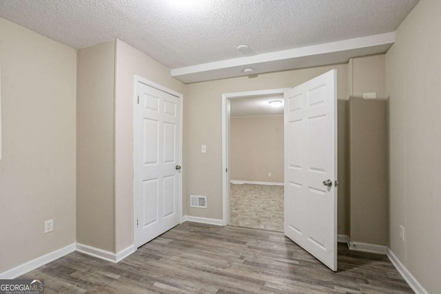 interior space with a textured ceiling, wood finished floors, visible vents, and baseboards