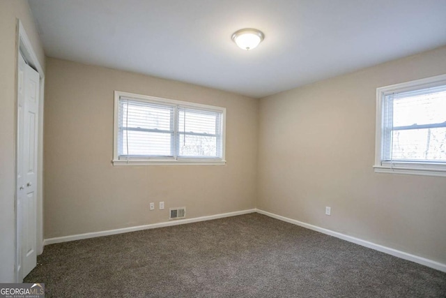 unfurnished bedroom with baseboards, multiple windows, visible vents, and dark colored carpet