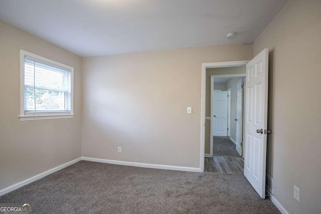 empty room featuring dark colored carpet and baseboards