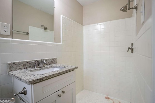 bathroom with a tile shower, vanity, and tile walls