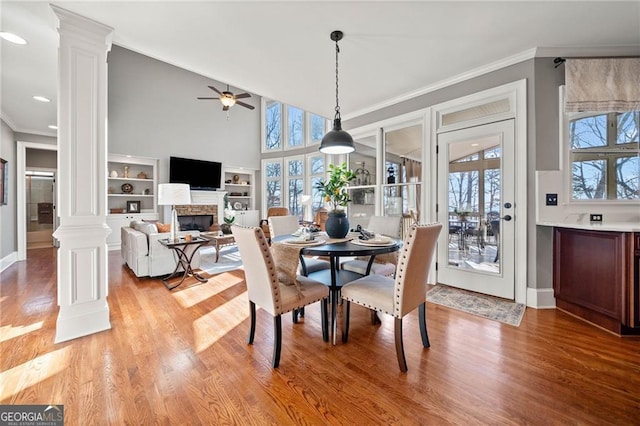 dining room featuring light wood finished floors, a fireplace, crown molding, and ornate columns