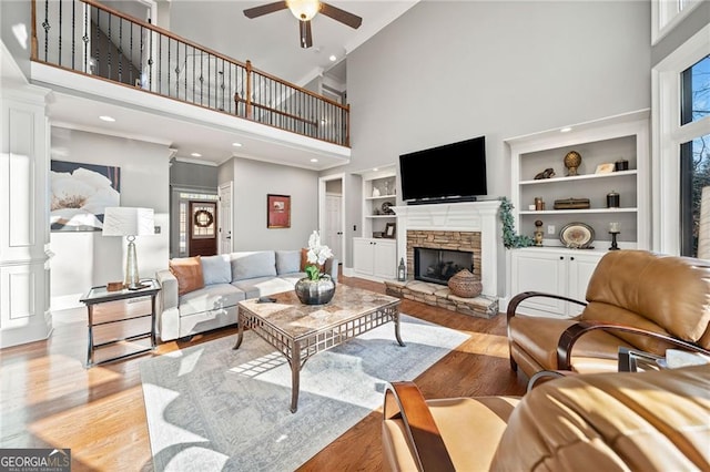 living area with built in features, a wealth of natural light, a stone fireplace, and wood finished floors