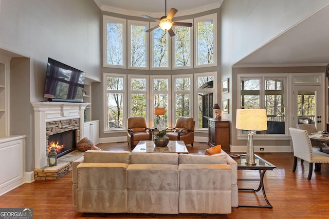 living area with built in features, a wealth of natural light, a stone fireplace, and wood finished floors
