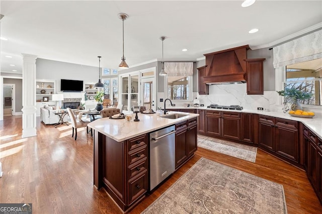 kitchen with a sink, stainless steel appliances, a fireplace, decorative columns, and custom exhaust hood