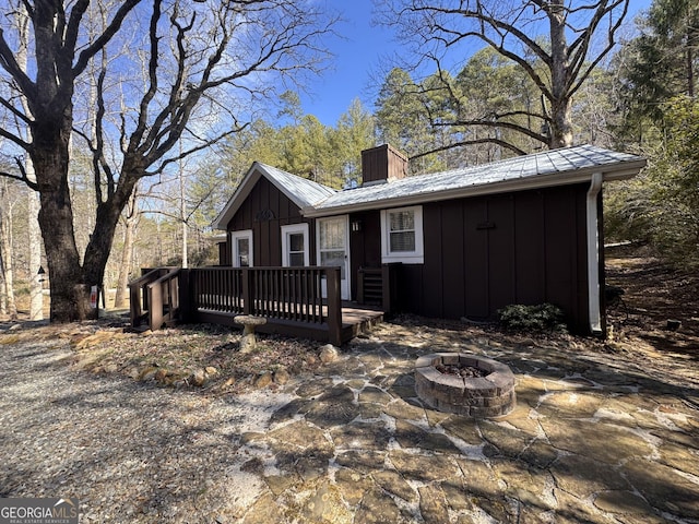 view of front of property with a fire pit, a chimney, metal roof, a deck, and board and batten siding