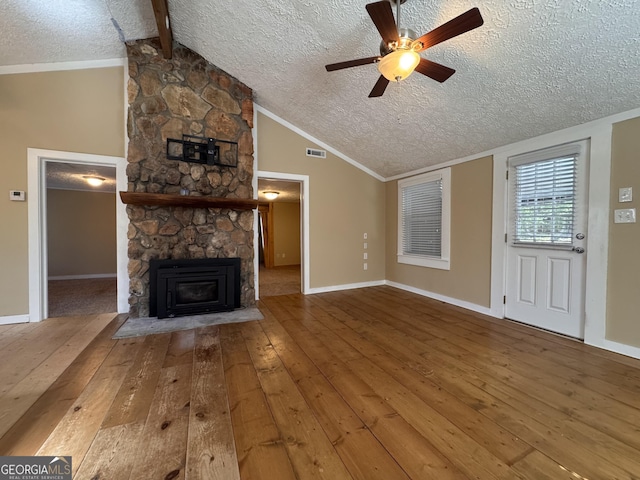 unfurnished living room with lofted ceiling with beams, a stone fireplace, a textured ceiling, and hardwood / wood-style flooring