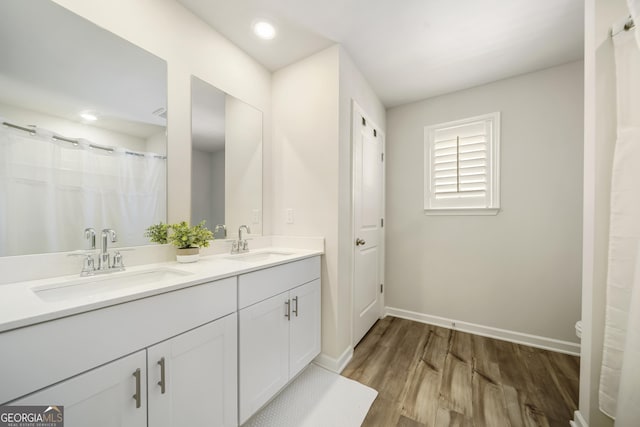 full bath featuring double vanity, wood finished floors, baseboards, and a sink